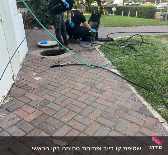 עובדים עם ציוד ליד פתח ביוב